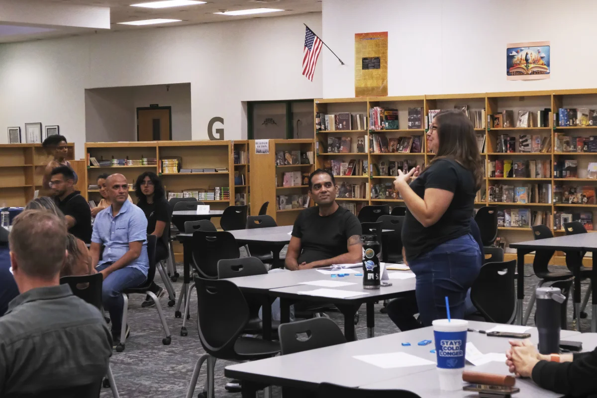 A Gilbert Toastmasters member speaking to fellow members seated around tables in the Greenfield Junior High library